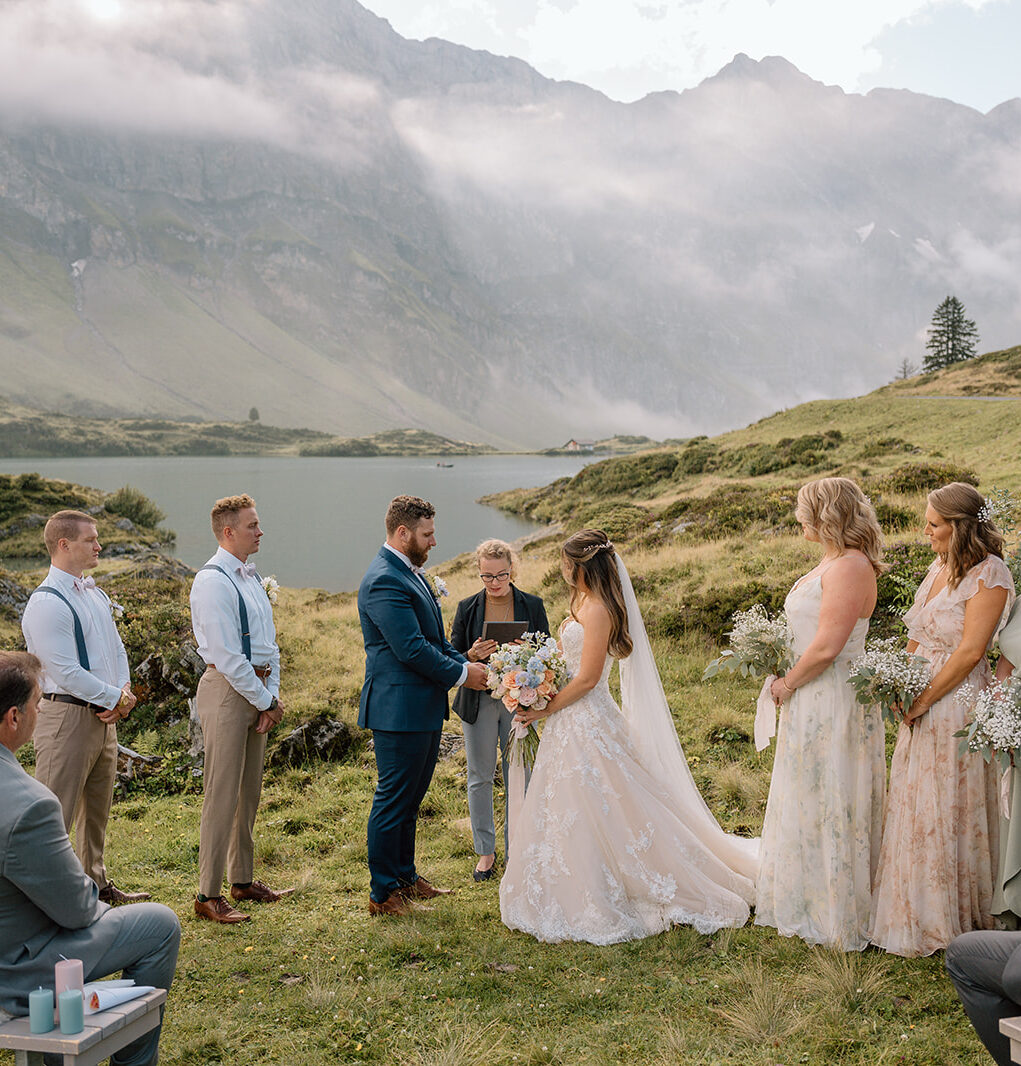 Couple at their intimate wedding ceremony at Trübsee in Engelberg, Switzerland, couple in the foreground with their wedding party, the lake and green meadows and mountains in the background