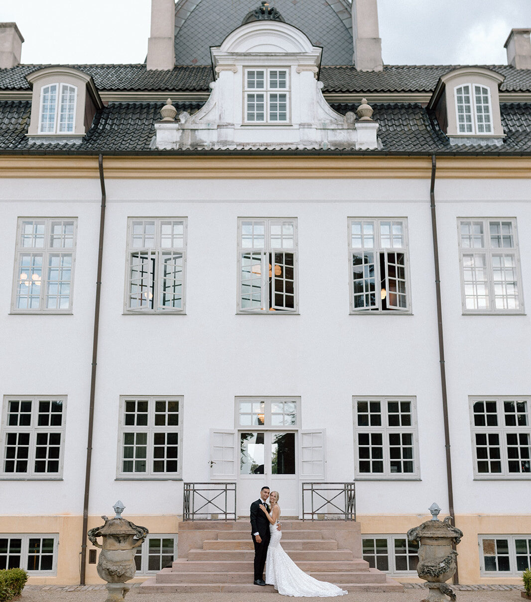 Bride and Groom on steps in front of Charlottenlund Slot Castle smiling at the camera for their wedding photos