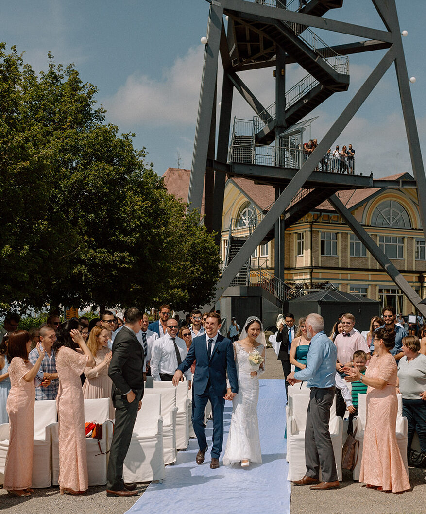 Wedding couple walking to their ceremony with their families and friends standingon the sides of the aisle applauding them at Uto Kulm Uetliberg Intimate Wedding in Zurich, Switzerland